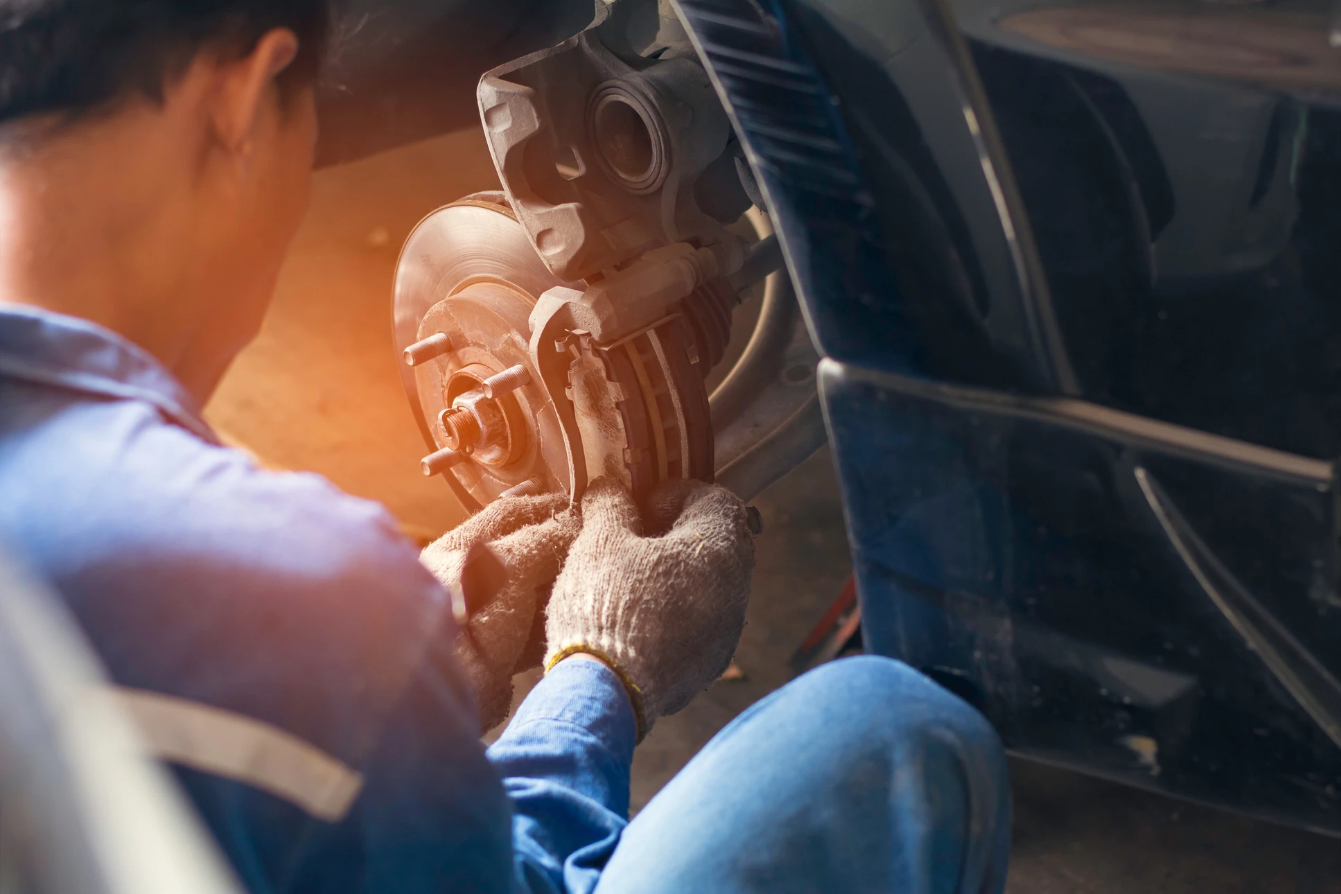 Mécanicien automobile travaillant sur système de freinage dans garage, portant gants de protection, manipulant étrier de frein et disque