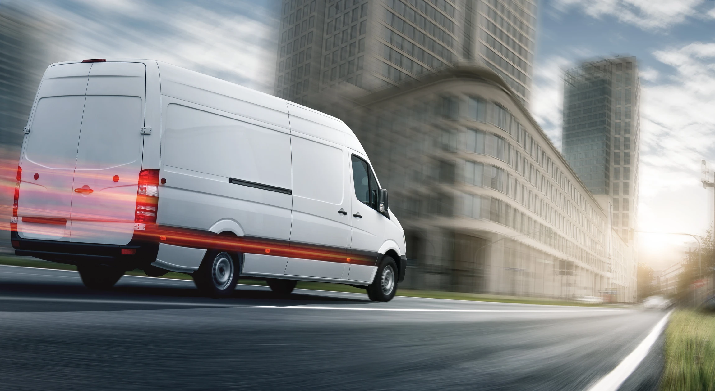 Camionnette utilitaire blanche en mouvement sur route urbaine, avec buildings modernes en arrière-plan flou