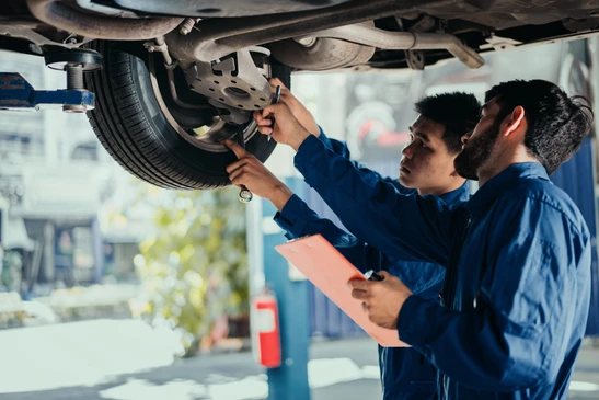 Deux mécaniciens automobiles en combinaisons bleues inspectent le dessous d'un véhicule surélevé dans un garage