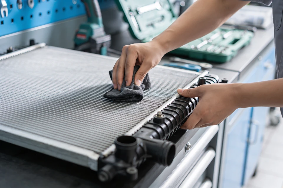 Photographie d'un vendeur ou responsable de magasin de pièces automobiles en conversation directe et attentive avec un client à l'intérieur du magasin. Le vendeur doit être clairement engagé dans une échange personnel (geste accueillant, posture d'écoute), dans un environnement de rayonnages de pièces automobiles (boîtes, composants mécaniques) visibles en arrière-plan. La scène doit transmettre la confiance, la proximité et la disponibilité personnalisée. Lumière naturelle ou lumière chaude intérieure. Photographie réaliste de niveau professionnel.