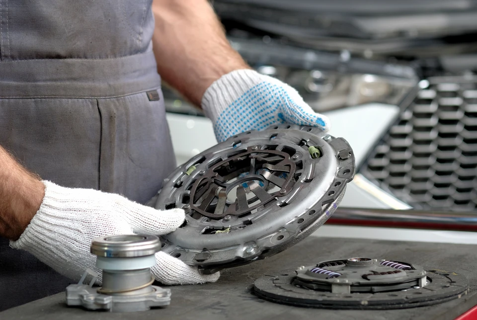 Intérieur accueillant d'un magasin de pièces détachées automobiles avec des rayonnages bien organisés présentant divers composants et pièces auto (moteur, freinage, filtres, courroies). Un vendeur professionnel en uniforme ou tenue professionnelle se tient derrière un comptoir, engagé avec un client particulier. L'ambiance doit transmettre la proximité, la confiance et le professionnalisme, avec un espace de travail moderne et bien entretenu typique d'un commerce de proximité automobile.